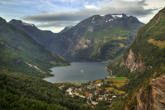 Aerial view of Geirangerfjord with steep green mountains, deep blue water, and a small village in Stranda Municipality, More og Romsdal, Norway.