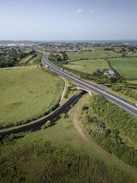 Aerial view of a highway crossing over a canal surrounded by green fields and trees with the town of Lancaster in the distance, Lancaster, England, United Kingdom.