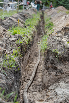 Workers are installing a high voltage cable in a trench filled with soil and grass. The area shows signs of construction activity and preparation