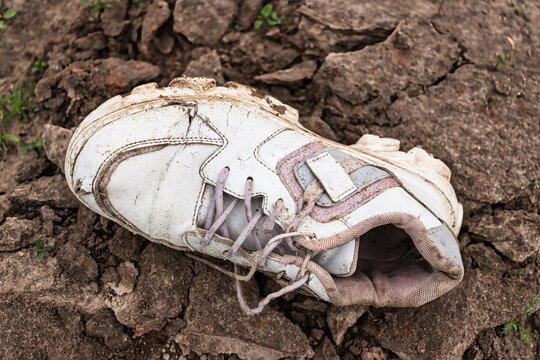 Worn white sneaker resting on cracked earth in an abandoned area during the afternoon