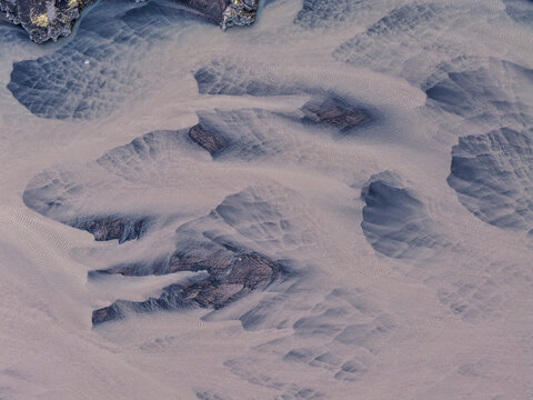 Aerial view of volcanic black sand dunes with intricate wind-blown patterns and dark rocky outcrops in the landscape of Thykkvabaejarklaustur, Skaftahreppur, Iceland.