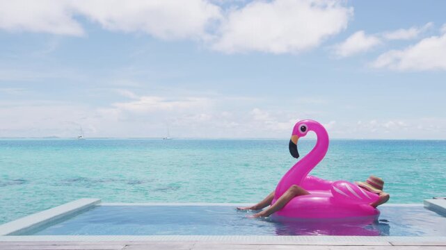 Travel vacation holidays concept. Woman in pool by beach relaxing in bikini in inflatable pink flamingo toy mattress float relaxing in luxury. Raw vertical video of real woman model without makeup
