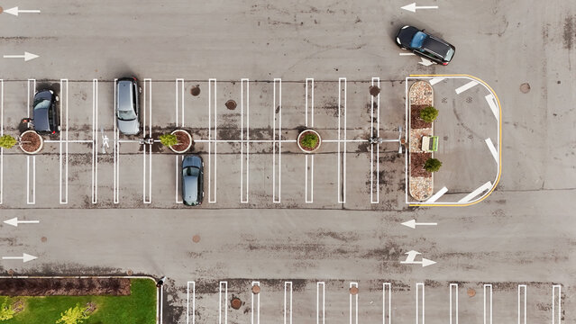 Aerial view of a parking lot with parked cars, white parking space markings, and small trees in circular planters in Riga, Latvia.