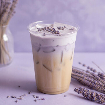 Iced lavender latte in a clear plastic cup with purple foam topping and dried lavender sprigs on a soft purple background