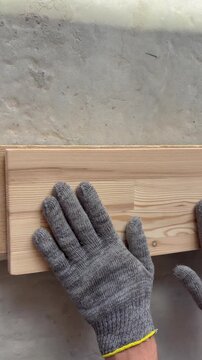 A worker's gloved hand checking the smoothness of a sanded wooden board. Woodworking, or home renovation
