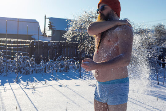 A bearded man practices cold exposure by rubbing snow on his body