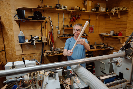 Candid woodworker holding turned dowel in rustic workshop