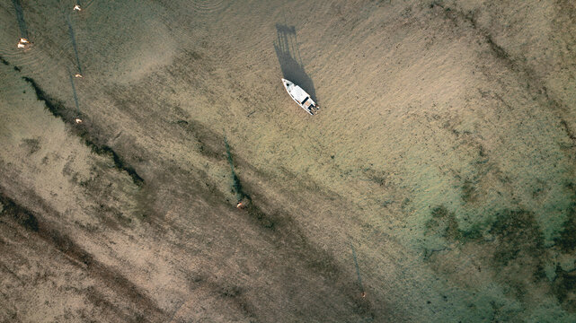 Aerial view of a small boat anchored in the shallow, clear waters off the coast of Gili Trawangan with people wading nearby in Pemenang, West Nusa Tenggara, Indonesia.