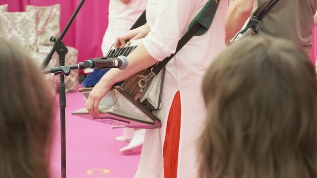 musician playing harmonium during live kirtan performance. devotees dancing hare krishna during spiritual kirtan. joyful kirtan creates peaceful atmosphere for spiritual group gathering