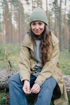 Woman sitting on a fallen tree and looking at the camera with a gentle smile during a quiet forest break, enjoying a relaxed outdoor lifestyle in nature