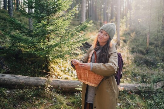 Young woman enjoying mushroom foraging in a sunlit forest, holding a traditional wicker basket while exploring nature during a peaceful outdoor activity.