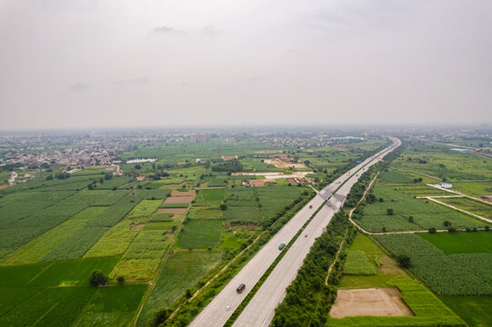 Aerial view of the Eastern Peripheral Expressway cutting through lush green agricultural fields and rural landscape in Sonipat, Haryana, India.