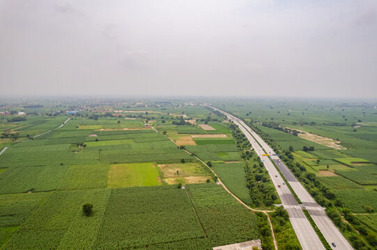 Aerial view of the Eastern Peripheral Expressway cutting through lush green agricultural fields and farmland in Sonipat, Haryana, India.
