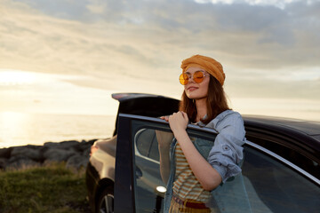 Fototapeta premium woman lifestyle fashion travel sunset outdoors car, Smiling woman by a car at sunset wearing denim jacket striped dress hat and sunglasses, an outdoor lifestyle moment