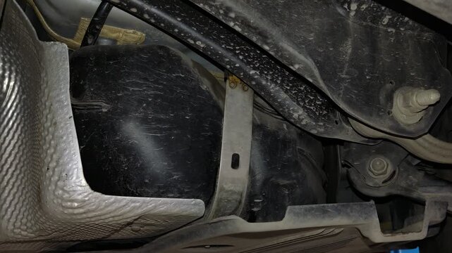 A black plastic fuel tank secured with a metal strap underneath a car.