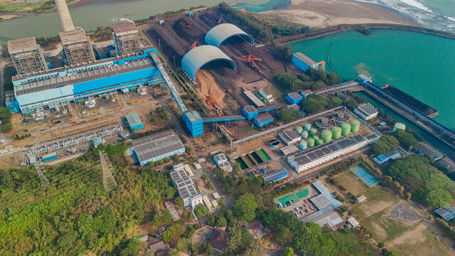 Aerial view of a large coal-fired power plant facility featuring coal storage domes, conveyor belts, and industrial infrastructure situated along the coast
