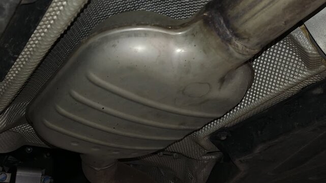 A metal car exhaust muffler or resonator located underneath the vehicle chassis.