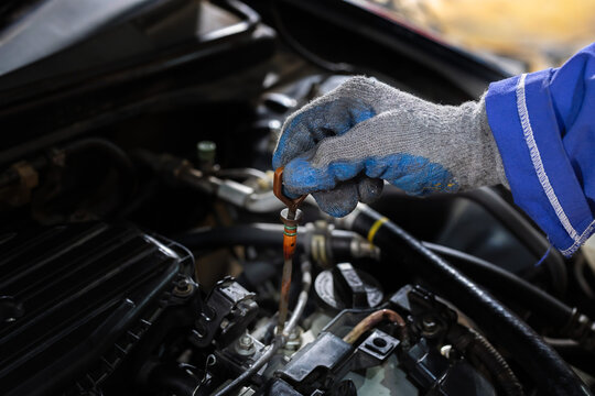 Worker checks oil level in car engine during maintenance session in garage