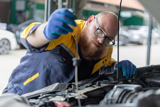 Worker checks oil level in car engine during maintenance session in garage