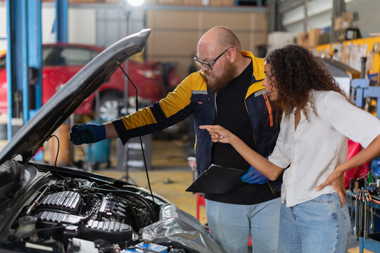 Mechanic checks car engine while customer looks on inside auto repair shop