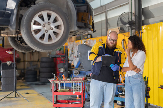 Mechanic checks car engine while customer looks on inside auto repair shop
