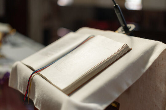 A religious ceremony takes place in a catholic church with an open holy bible on the altar. The community gathers in prayer and worship.
