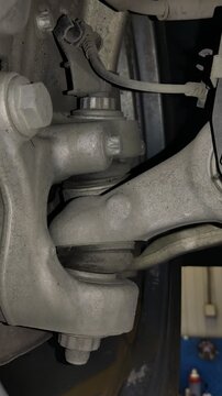 A close-up view of a car front suspension steering knuckle connected to control arms with ball joints and electrical wiring sensor.