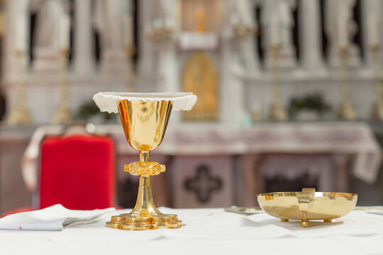 A holy mass takes place in a catholic church with an altar. A golden chalice and dish are prepared for the ceremony.