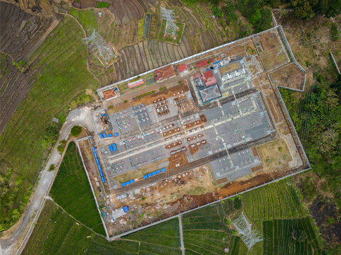 Aerial view of the Hydroelectric Jelok Tuntang power plant surrounded by lush green rice fields and power transmission lines in Tuntang, Central Java, Indonesia.