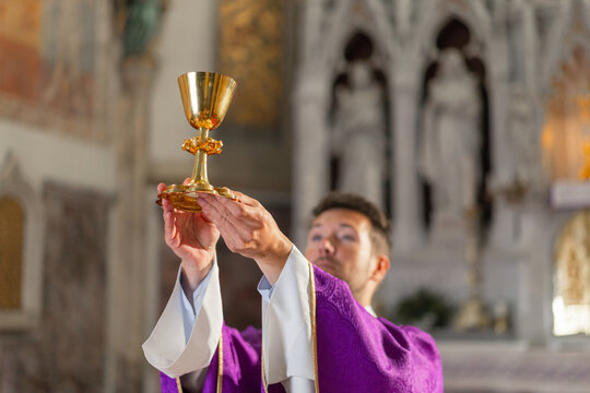 A catholic priest raises the chalice during a religious ceremony in a church in Europe. The congregation watches in reverence.