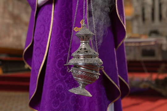 A catholic priest conducts a holy mass in a church in Europe. Incense pours from a metal container as part of the service.