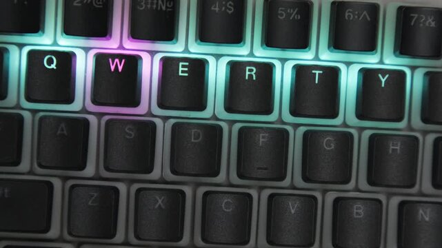Top view of computer keyboard with QWERTY layout and LED backlighting in dark room close-up