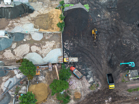 Aerial view of an industrial construction site with piles of sand, gravel, and soil, featuring heavy machinery including excavators and dump trucks, in Dhaka, Dhaka Division, Bangladesh.