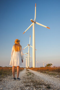 Woman Facing Wind Turbines Along Rural Gravel Path