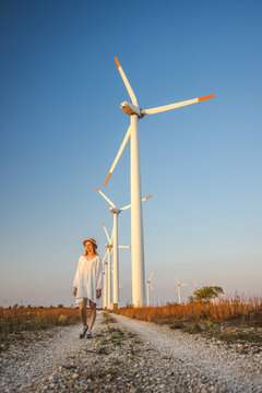 Woman Walking Along Gravel Path Through Rural Wind Farm