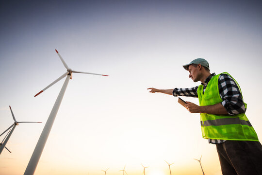 Wind Energy Worker Pointing Toward Turbines at Sunset