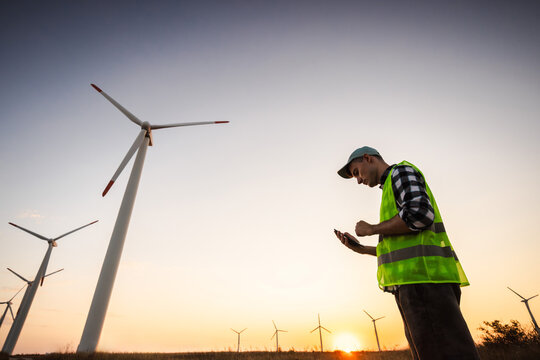 Wind Farm Worker Checking Smartphone Among Turbines at Sunset