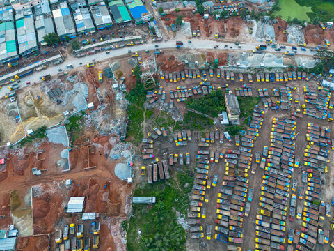 Aerial view of a large construction site featuring rows of parked yellow trucks and piles of earth and gravel in Dhaka, Dhaka Division, Bangladesh.