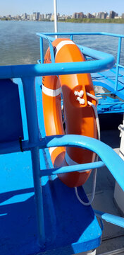 Vertical view of an orange life ring secured to a blue metal railing on a passenger boat deck over water. Marine adventure and water safety concepts 