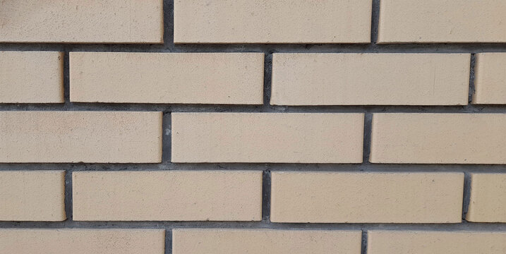 Texture of a clean light beige brick wall with dark grout lines in a horizontal pattern. 