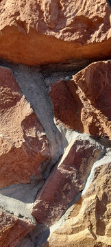 Texture of a natural stone wall composed of large orange and brown jagged rocks held by concrete mortar. 
