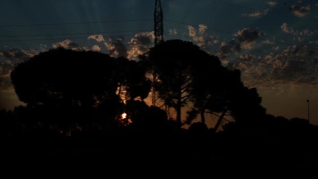 Scenic view from a moving train window showing a beautiful sunset over a silhouetted landscape. The sun's golden rays shine through clouds