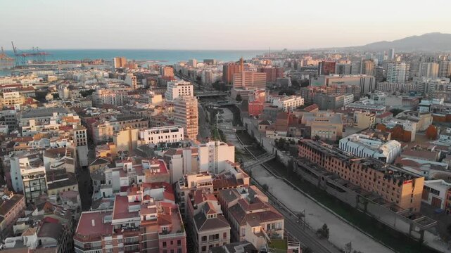 Gliding over Malaga's urban sprawl and river towards the Mediterranean Sea at golden hour, showcasing coastal development and future potential, inspiring investment and exploration.