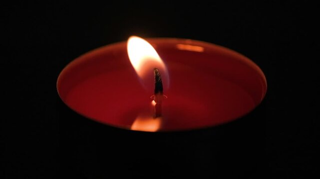 Red tealight candle flame slowly flickering and burning out in complete darkness, close-up atmospheric footage