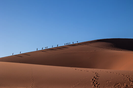 Hikers trekking up a desert sand dune in Namibia