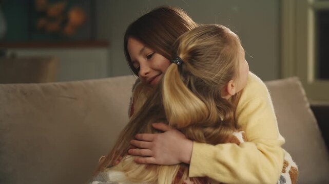 Smiling girl hugs her little sister at home, showing family love and support