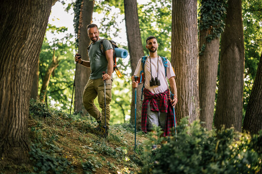 Two male hikers walking through a lush forest with backpacks and trekking poles