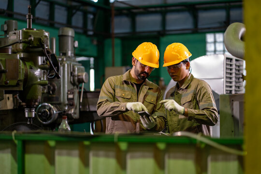 Team of industrial worker is checking the setup value of  metal casting machine by automated monitor while working inside roof factory for safety industry