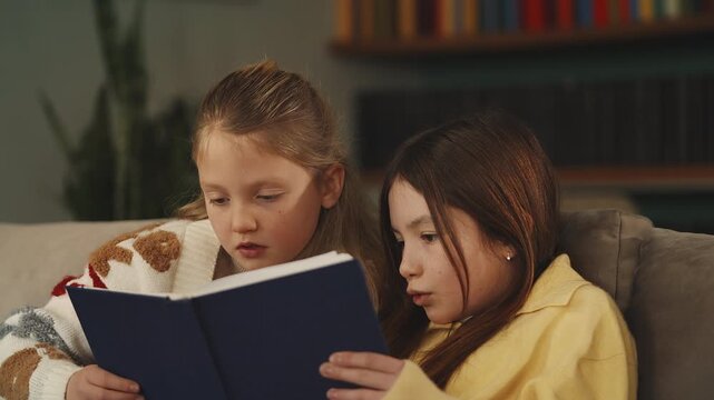 Two focused siblings read a book together, enjoying leisure time at home
