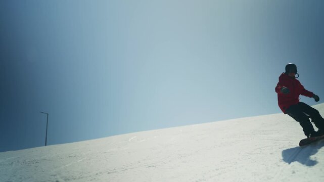A snowboarder in a red jacket gracefully descends a snow-covered mountain. Enjoying winter sports, the person carves down the slope under a clear blue sky.